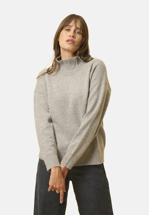 Lys grå strikket sweater med høj krave, ribbede manchetter og afslappet pasform, parret med mørke jeans. Blød tekstur, minimal detaljer.