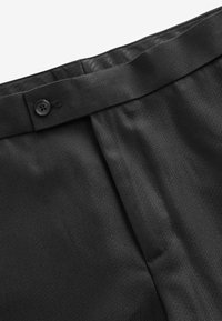 Pantalones negros con una tela texturizada, que presentan una cinturilla suave y un cierre de botón. Pliegues visibles cerca de la cintura.