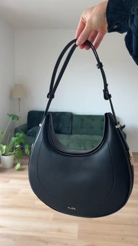 Sac à main en cuir noir avec une forme courbée, des poignées doubles et un logo doré. Texture lisse avec des éléments de design minimalistes.