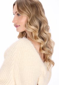 Crème-kleurige gebreide trui met een losse pasvorm, voorzien van een diepe V-hals aan de achterkant en een gestructureerde stof. Zachte, pluizige textuur met subtiele details.