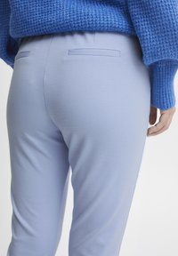 Helleblaue, elastische Hosen mit glatter Textur und zwei Gesäßtaschen. Neben einem gestrickten, leuchtend blauen Pullover präsentiert.