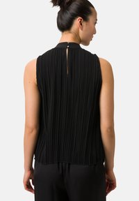 Svart plisserad ärmlös topp med hög krage och knappstängning bak. Slät textur, flödande tyg och avslappnad passform.