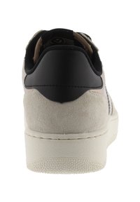 Baskets lacées avec un talon en cuir noir et un dessus en daim beige. Présente une semelle blanche texturée et un logo subtil sur la languette.