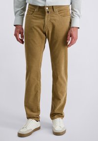 Beige Cordhosen mit geradem Schnitt, ausgestattet mit zwei Vordertaschen, einem Knopfverschluss und einer glatten Textur, kombiniert mit weißen Sneakers.