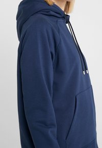 Felpa con cappuccio di colore blu navy, dotata di cappuccio regolabile, tasca laterale e polsini a coste. Realizzata in un morbido tessuto testurizzato. Design semplice.