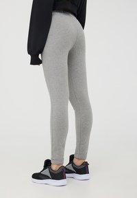Leggings grigi con un design aderente e una cintura elastica, abbinati a scarpe da ginnastica nere e viola con dettagli in rete.