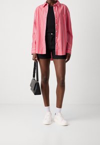 Red and white striped long-sleeve shirt over a black tank top, paired with black shorts and white sneakers. A small black handbag is held.