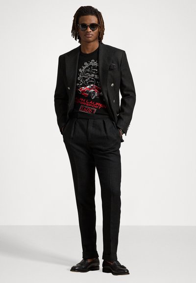 Veste de costume noire à double boutonnage sur un t-shirt graphique avec un design de voiture rouge, assortie à un pantalon ajusté et des chaussures noires, rehaussée d'un mouchoir de poche.