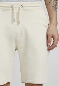 Cremefarbene Baumwollshorts mit verstellbarem Bund, seitlichen Taschen und genähten Säumen. Sie verfügen über eine glatte, weiche Textur und eine lässige Passform.