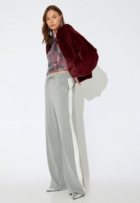 Bordeaux faux fur hoodie, bedekte grafische top met pailletten, grijs gestreepte wijde broek met witte zijkanten en metallic puntige schoenen.