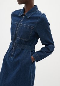 Denim jurk met een kraag, ritssluiting aan de voorkant, elastische taille, lange mouwen en twee borstzakken in donkerblauw.