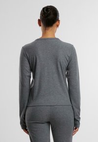 Šedý dlouhý rukávový top s ribovanou texturou, kulatým výstřihem a přiléhavým střihem. V kombinaci s odpovídajícími šedými kalhotami pro jednotný vzhled.