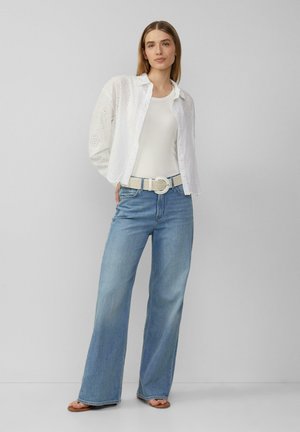 Witte eyelet shirt over een crèmekleurig tanktop, gecombineerd met hoog- taille lichtblauwe wijde jeans en een geweven witte riem met een ronde gesp.