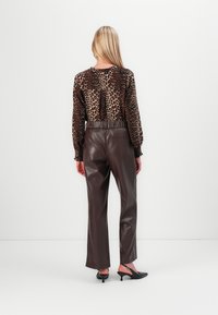 Blouse à imprimé léopard avec des manches longues, des poignets élastiques, et un détail de lien dans le dos, associée à un pantalon en simili cuir marron taille haute.