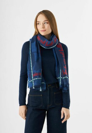 Écharpe bleu marine en tissu doux, ornée de texte rouge et de motifs géométriques, avec des bords frangés et un design en couches.