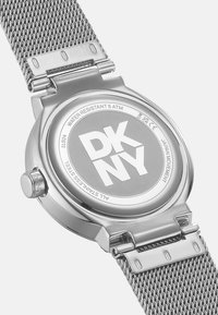 Silberner Edelstahl-Uhren mit einem Netzarmband. Verfügt über ein rundes Gehäuse auf der Rückseite, das "DKNY" anzeigt, und ist bis zu 5 ATM wasserdicht.