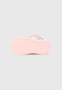 Suela de zapato rosa con surcos texturizados, presentando una ligera curva. Detalle con letras coloridas impresas en el lateral. Material suave visible.