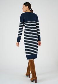 Abito lavorato a maglia a strisce navy con maniche lunghe, caratterizzato da strisce orizzontali bianche. Abbinato a stivali alti in suede marrone. Texture liscia, lunghezza al ginocchio.