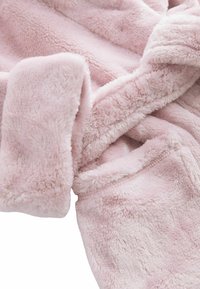 Flauschiger pinkfarbener Stoff mit einer weichen Textur, der ein Falten- und Nahtdetail aufweist. Das Material wirkt gemütlich und warm, ideal für Freizeitkleidung oder Decken.