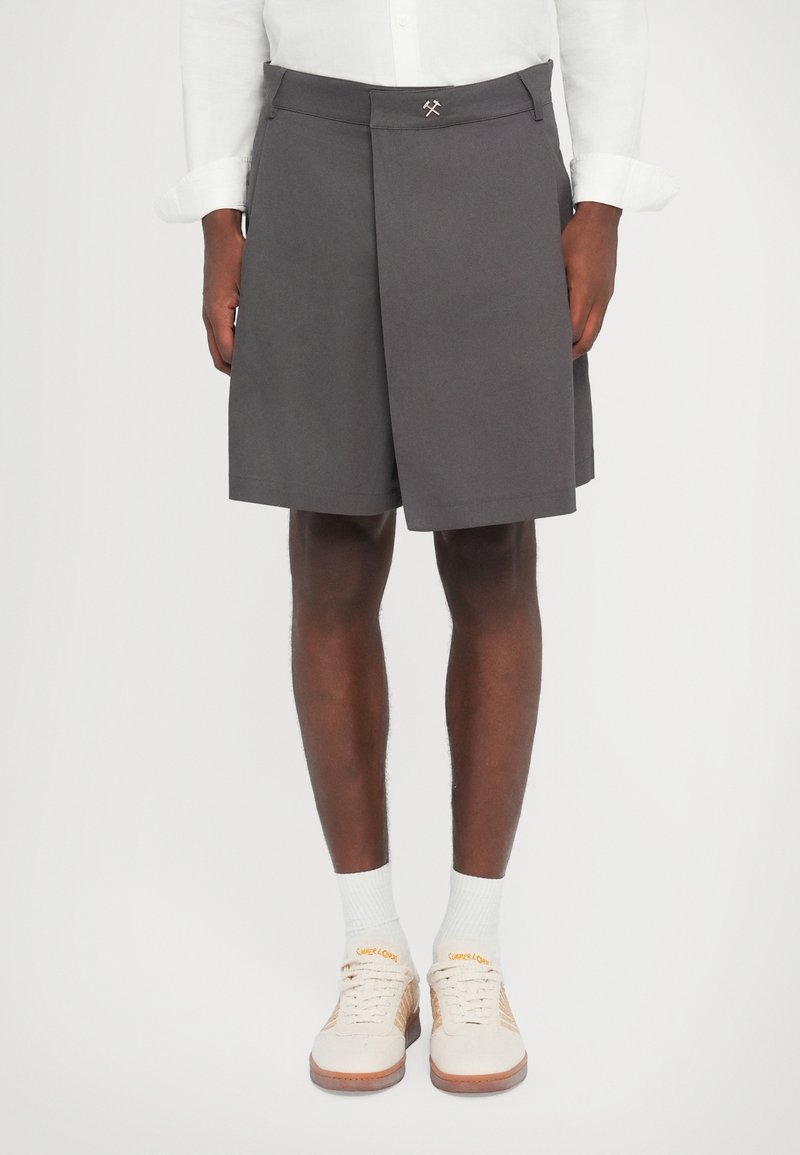 Shorts gris avec une devant plissé et une taille plate. Associés à des baskets beige clair et des chaussettes blanches. Design simple avec peu de détails.