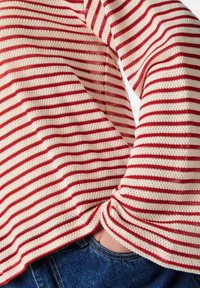 Maglione a righe rosse e bianche realizzato in tessuto testurizzato, con maniche lunghe e orlo arrotondato. Indossato sopra un denim blu.