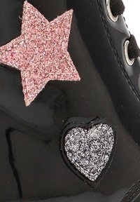 Calzado de charol negro con una estrella de purpurina rosa y un corazón de purpurina plateada. El diseño incluye cordones y ojales negros.