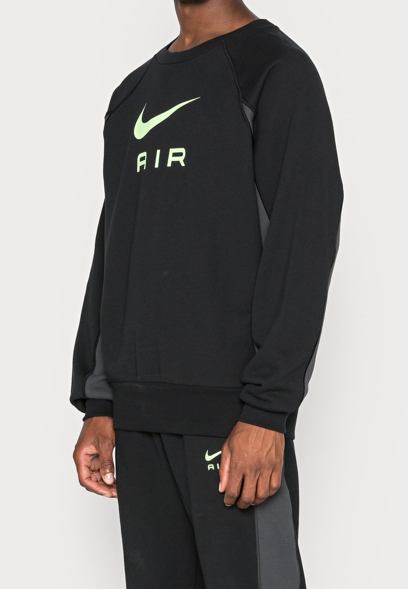 Svart sweatshirt med rund halsringning, med en stor grön Nike-logotyp och ordet "AIR." Inkluderar grå sidopaneler och strukturerat tyg.