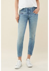 Ljust blå skinny jeans med hög midja, med knäppning och dragkedja, två framfickor och en cropped nederkant. Vita sneakers bärs.