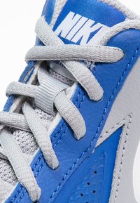 Niebieskie i szare sneakersy z teksturowaną skórzaną cholewką, siateczkowym wyściółką, wyraźnym logo Nike oraz płaskimi sznurowadłami. Akcenty obejmują przeszycia i perforacje.