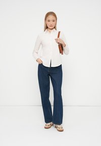 Camisa de botones rosa claro, de manga larga, combinada con jeans de pierna ancha azul oscuro. Correa de bolso color beige con herrajes, calzado estampado en la parte inferior.