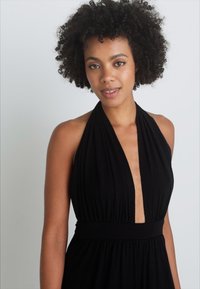 Melna halter stila kleita ar dziļu V veida kakla izgriezumu, savilktu augšu un platām jostām. Izgatavota no mīksta materiāla, ar pieguļošu siluetu.