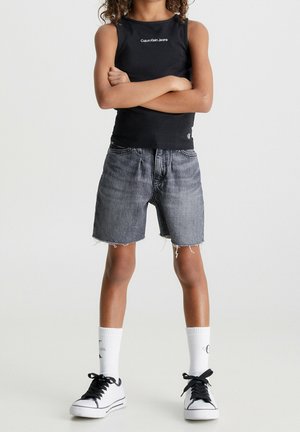 Top negro sin mangas con el logo de "Calvin Klein Jeans", pantalones cortos de mezclilla gris con dobladillo deshilachado, calcetines blancos y zapatillas negras. Un atuendo simple y casual.