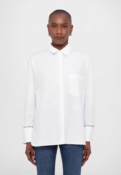 Chemise blanche à boutons avec col, poche poitrine unique et accents colorés à motifs sur les poignets. Tissu doux, coupe décontractée.
