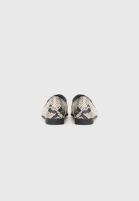 Chaussures imprimées serpent avec un motif texturé beige et noir, petit talon, bout arrondi et col élastiqué pour un enfilage facile.