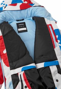 Bunte Jackeninnenausstattung mit einem hellblauen Futter, einer schwarzen Netztasche, roten und blauen Akzenten sowie einem auffälligen Markenlabel in der Mitte.
