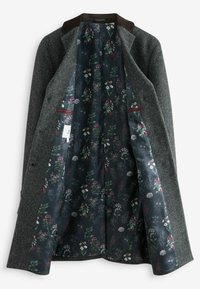 Grå tweedfrakke med en brun fløjelkrave, der afslører en mørk bund med blomstermønster. Har to forlommer og knaplukning.