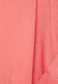 Korallfärgad tyg, slät textur, vikt med subtila sömnadsdetaljer, har lätta variationer i nyans och vävmönster.