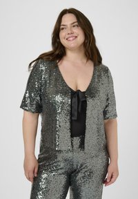 Glänsande metallic paljett jumpsuit i grått med korta ärmar, djup V-ringning och en rosettdekoration framtill. Mjuk textur och figurnära passform.