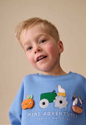 Svetlomodrá mikina s vyšívanými motívmi zeleného traktora, oranžovej farmárskej úrody, bielej kachny a kravy. Pod textom je nápis "MINI DOBRODRUŽSTVÁ ZÁBAVA NA FARME."