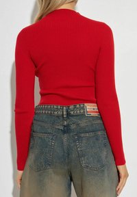 Top manica lunga rossa a coste abbinata a jeans denim blu a vita bassa con effetto sbiadito e un'etichetta vicino alla cintura con dettagli del marchio.