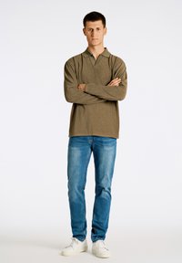 Polo a maniche lunghe a righe olive con colletto, abbinato a jeans slim-fit azzurri e sneakers bianche, crea un look casual.