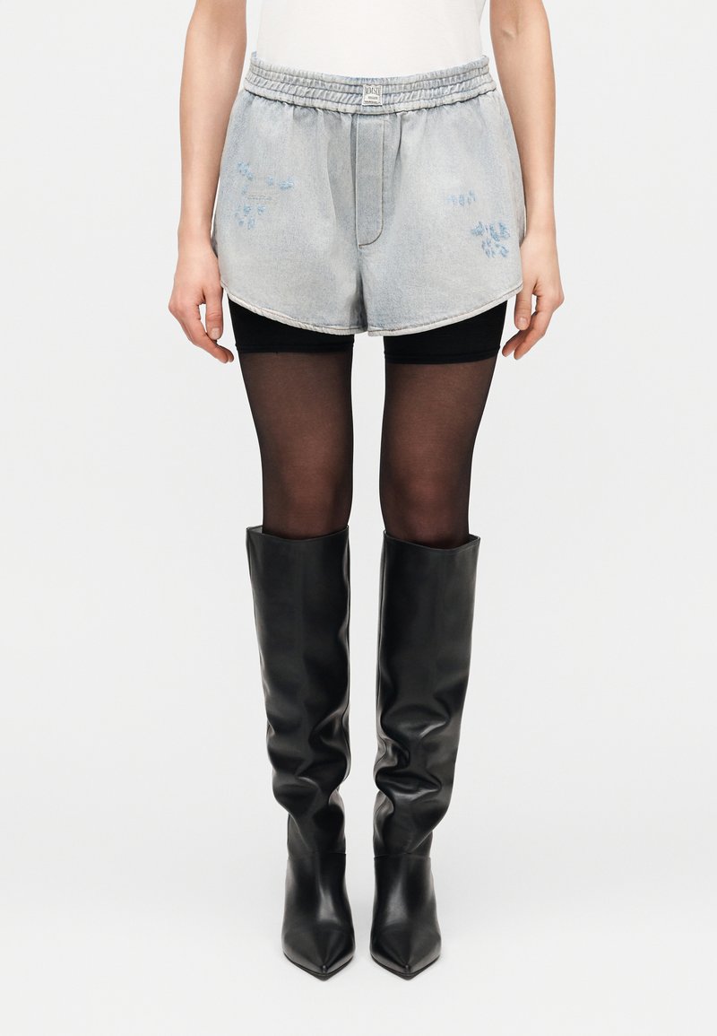 Džínsové krátke nohavice s elastickým pásom, svetlo modré, s modrou kvetinovou výšivkou; doplnené čiernymi koženými čižmami po kolená a pančuchami.