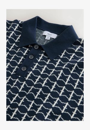 Tumesinine polo-särk valge geomeetrilise mustriga, kolmanda musta nööbiga ja ühevärvilise kraega. Valmistatud pehmest kangast, omab lõdvestunud istuvuse silti.