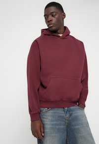 Hoodie bordeaux con tasca a canguro, polsini e orlo a coste. Realizzato in tessuto morbido, con cappuccio regolabile e vestibilità comoda.