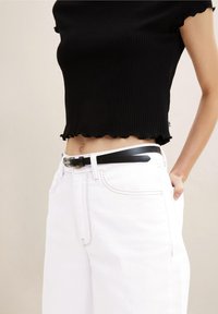 Svart ribbat crop top med scalloped nederkant, parat med vita högmidjade jeans, som har ett tunt svart bälte med en silverfärgad spänne.