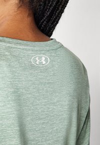 Grønn melert treningstrøye med rund hals og en hvit logo på ryggen. Myk tekstur med en avslappet passform.