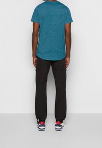 Tmavé cargo kalhoty s bočními kapsami v kombinaci s texturovaným tyrkysovým tričkem. Tenisky s červenými a modrými akcenty dokončují tento outfit.