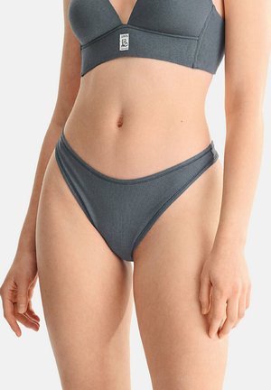 Gros plan d'une personne portant un ensemble soutien-gorge côtelé gris foncé assorti et culotte taille haute sur un fond clair uni.