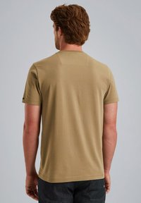 Khaki tričko s krátkým rukávem, kulatým výstřihem a malou obdélníkovou nášivkou na zadní straně. Materiál je hladký a těsně přiléhající k tělu.