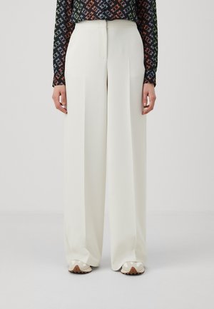 Pantaloni bianchi a gamba larga con una texture liscia e pieghe frontali sartoriali, abbinati a sneaker beige con suola testurizzata.